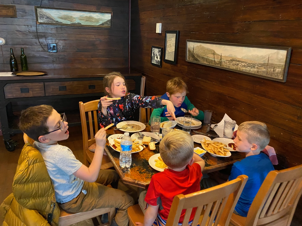 Children sitting at a table with plates of food in a rustic dining room