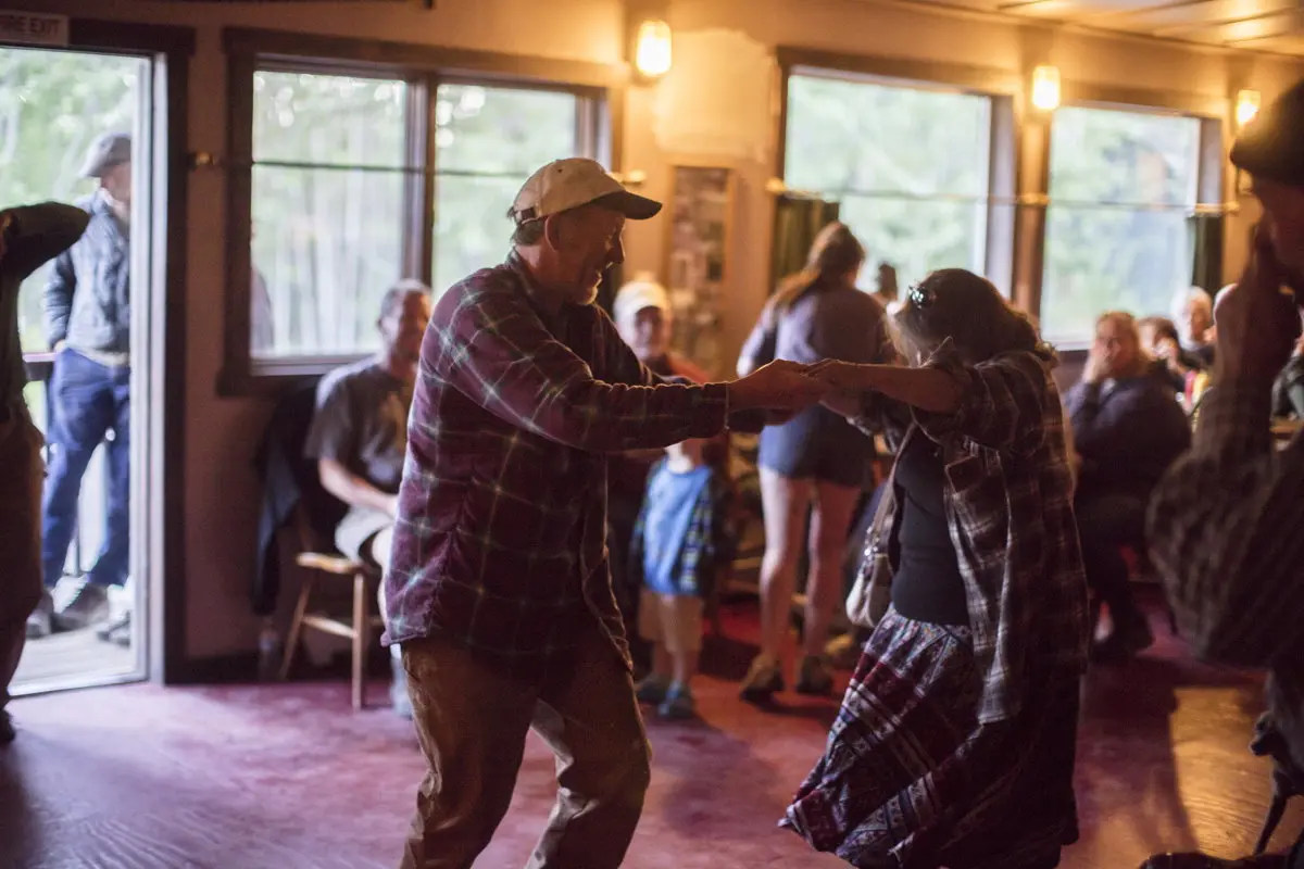 Two people dancing indoors with others in the background.