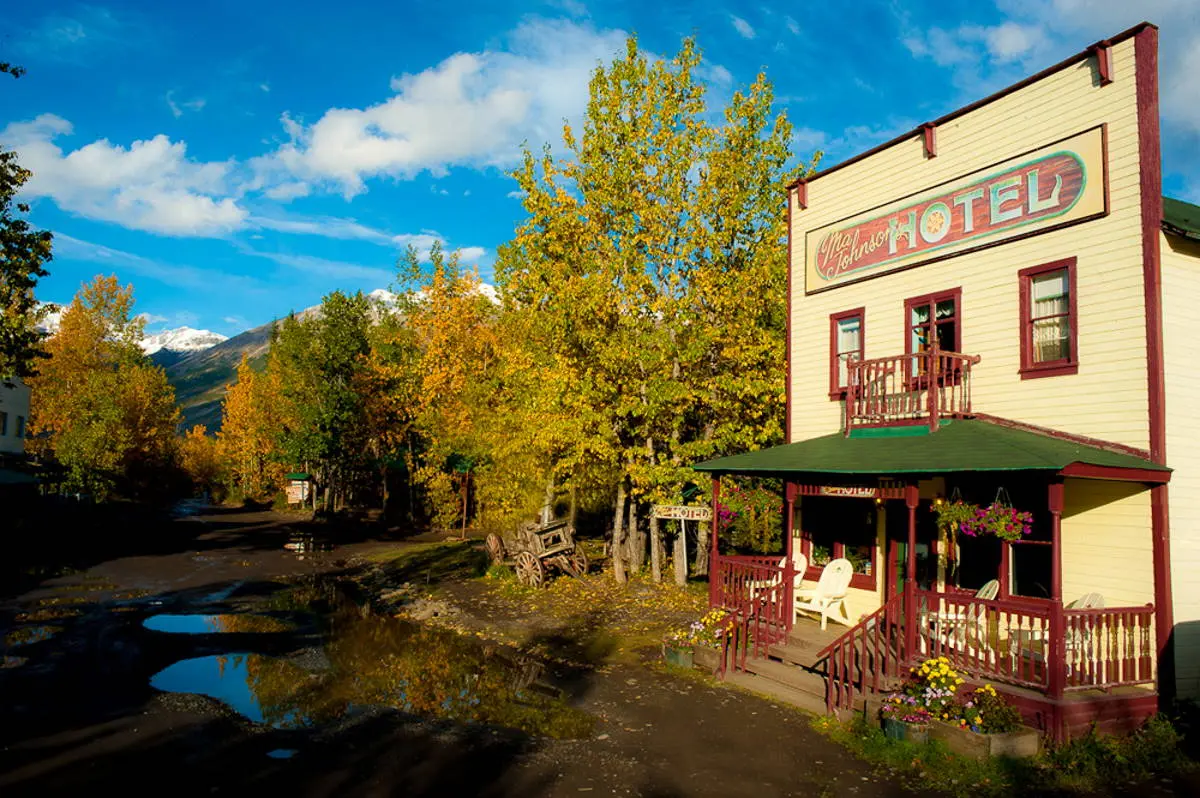 Quaint old-fashioned hotel with a porch, surrounded by autumn trees and mountain backdrop.