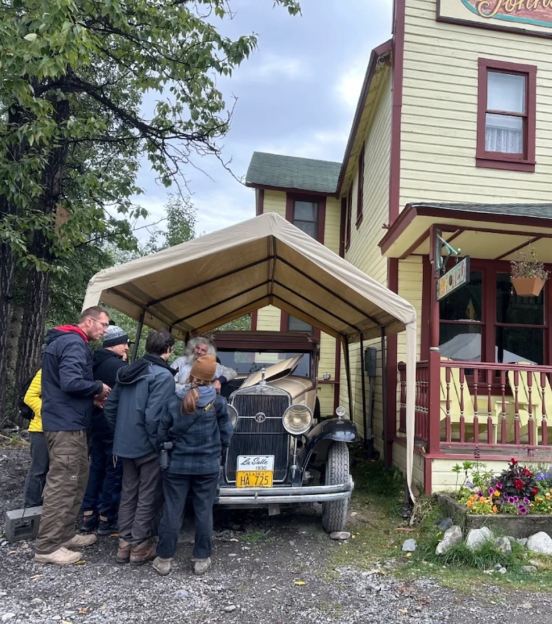 Group of people gathered around a vintage car parked under a canopy