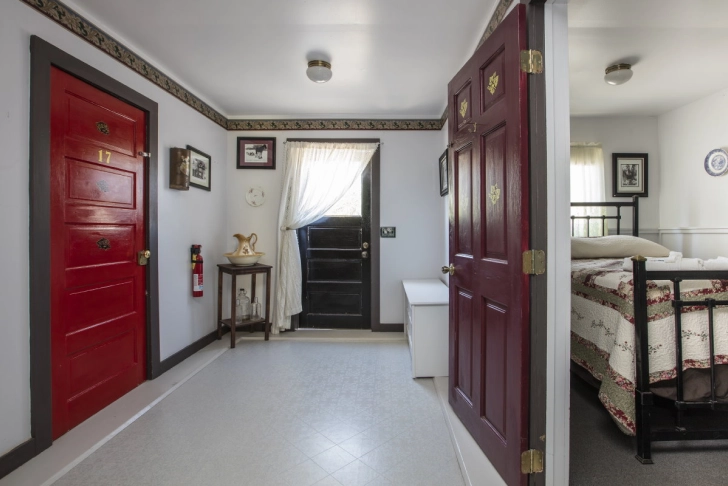 Vintage style bedroom with red doors, a bed with a quilt, and a small bathroom visible.