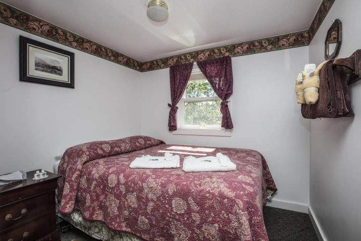 Cozy bedroom with a patterned bedspread, matching curtains, white walls with border trim, and a framed picture.
