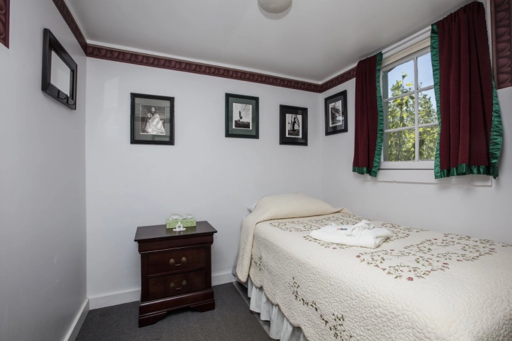 A tidy bedroom with a single bed, framed photos on the wall, and a nightstand.