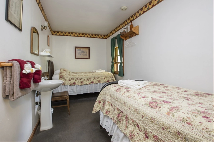 A small, quaint hotel room with two floral-patterned beds and a sink by the entrance.
