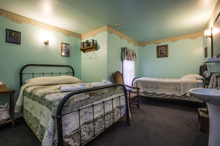 Quaint vintage bedroom with two beds and a sink, adorned with floral patterns and antique furniture.