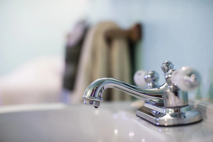 Chrome faucet with a water droplet, blurred background with hanging towels.