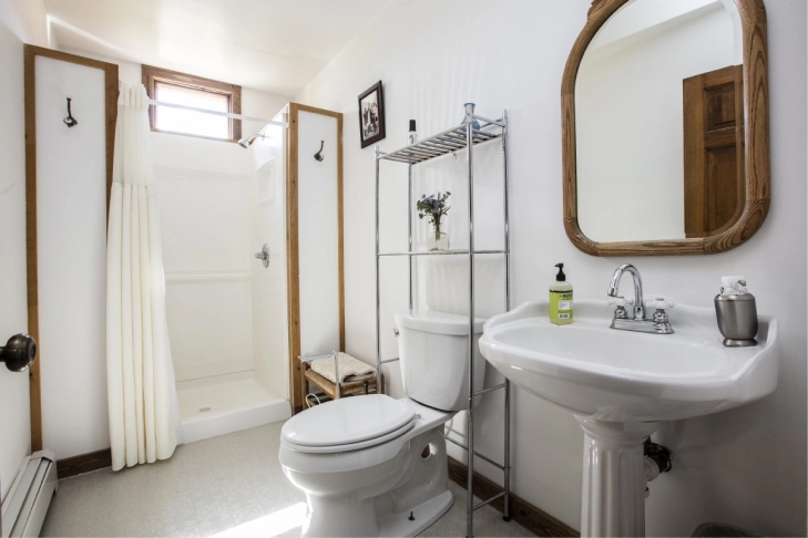 A bright, clean bathroom with a toilet, sink, mirror, and shower curtain.
