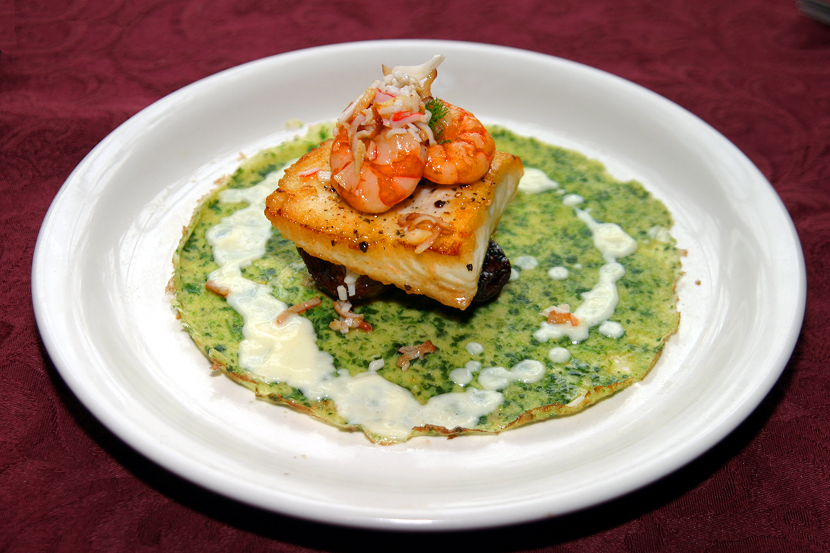 A plated dish featuring seared fish topped with shrimp and crab